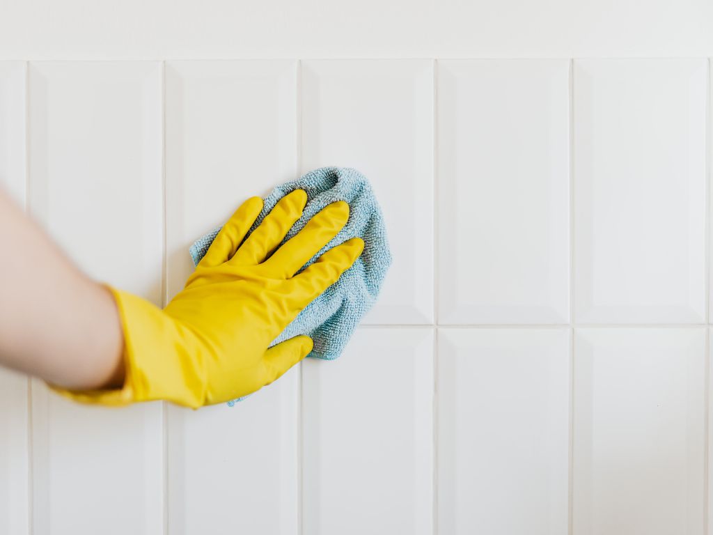 Une main avec gant qui nettoie le mur avec un chiffon